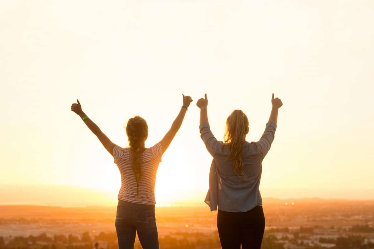 two girls holding up arms in the sunset