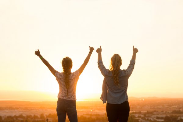 two girls holding up arms in the sunset